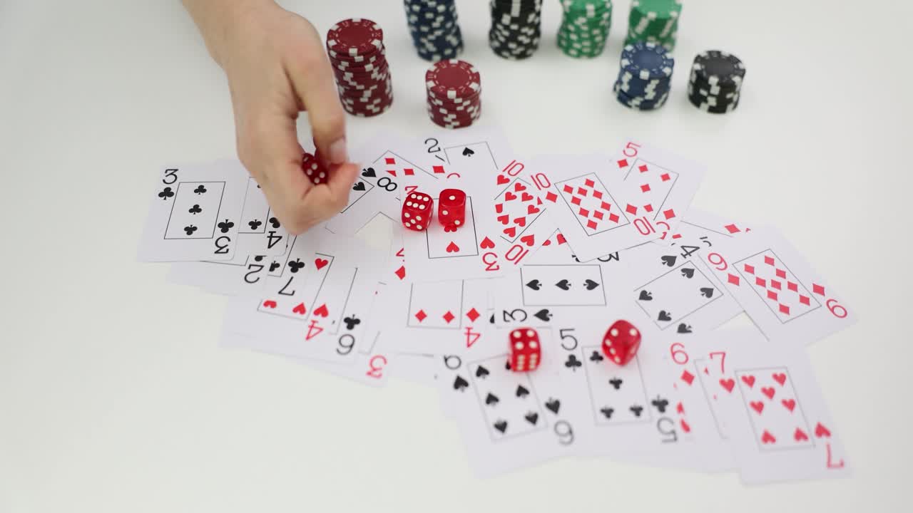 A hand interacts with playing cards and dice on a table, with poker chips in the background, depicting a gambling or game scene