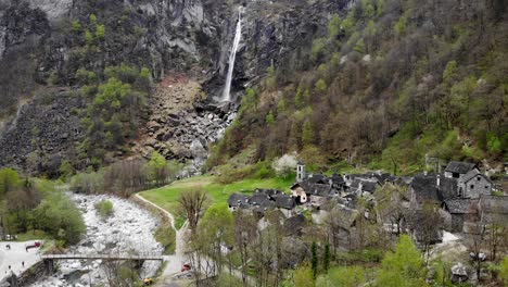 sobrevuelo aéreo sobre el pueblo de foroglio en ticino, suiza, con vistas a una de las cascadas más grandes de los alpes suizos en el fondo de antiguas casas de piedra