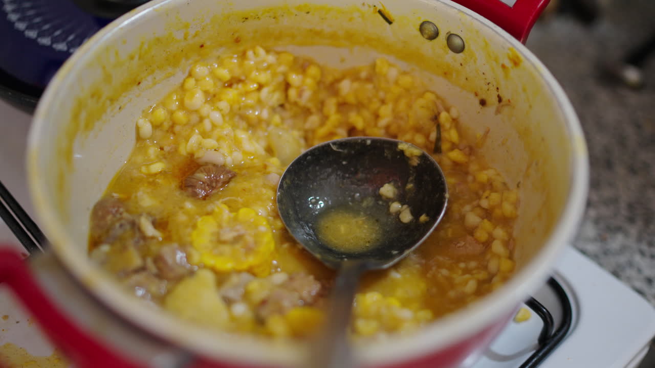 Close-up view of the popular Locro Argentino made from corn stew or potato during cooking in red pot with metal ladle.