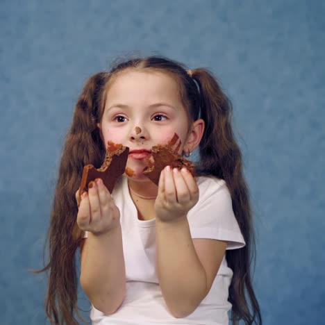 dirty face of a girl eating chocolate. two pieces of sweet chocolate in child's hands. portrait of a little kid with smeared face isolated in studio.