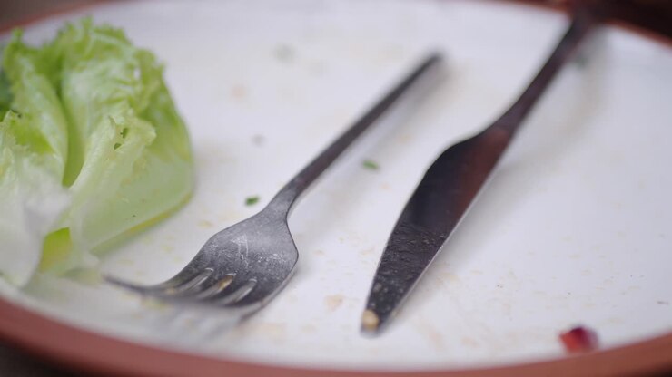 An empty plate with leftover salad and cutlery