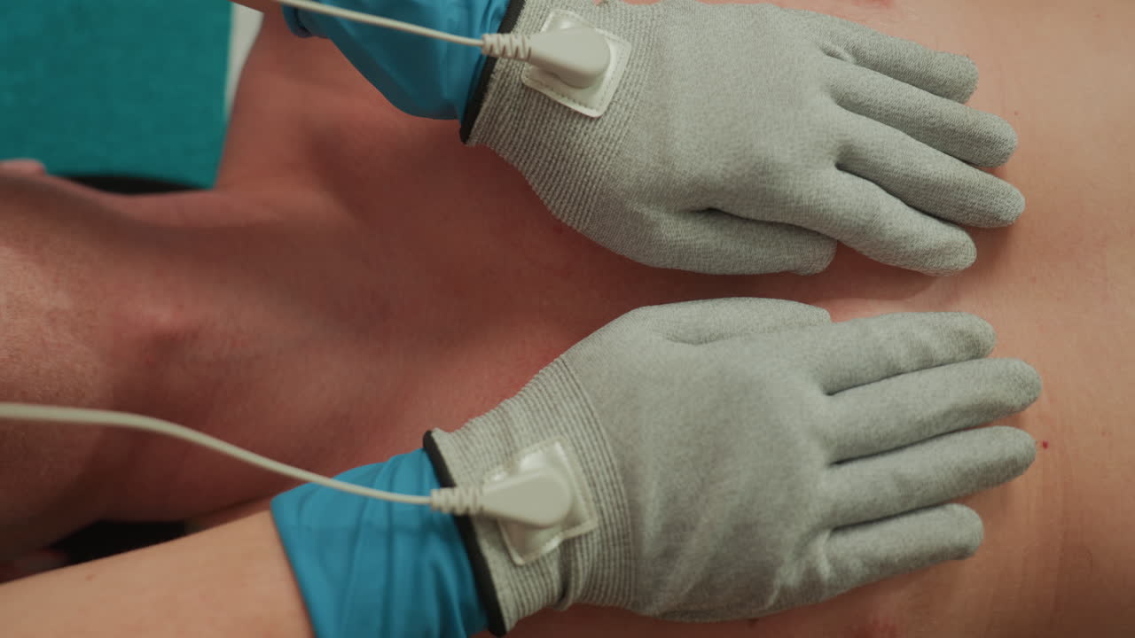 microcurrent chest massage with gloved hands on bare torso, esthetician applying electrode pads and gentle pulses, clinical spa atmosphere, soft ambient lighting, soothing relaxation treatment focused