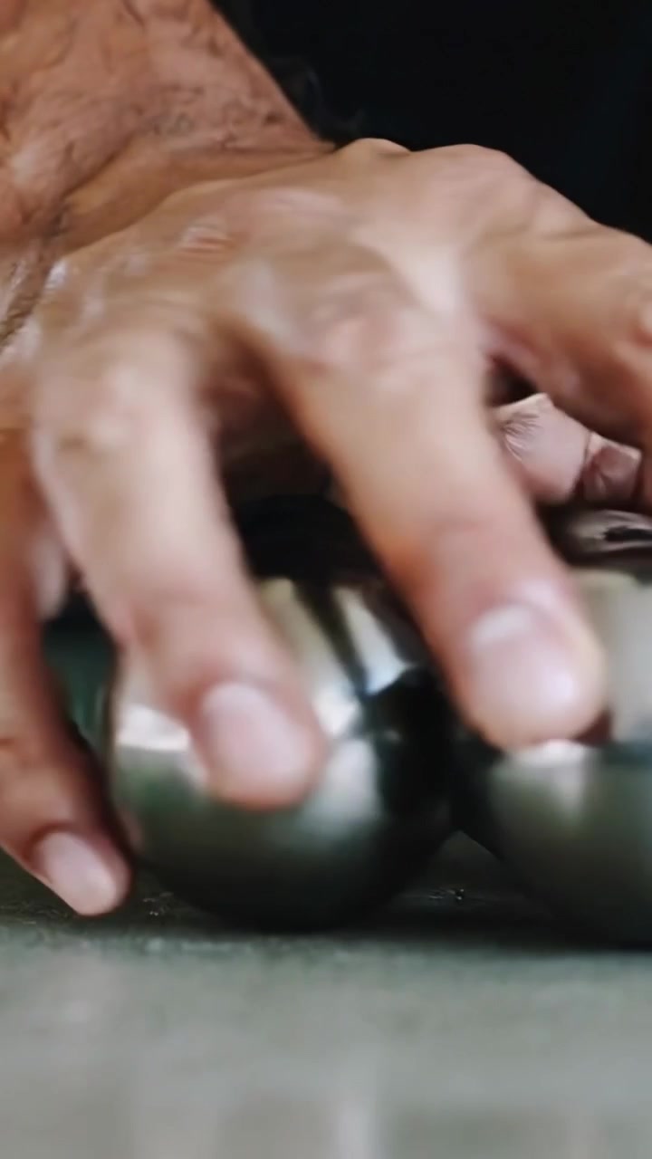 Vertical video: Reaching right hand in dark sleeve rolling two steel spheres on table holding them