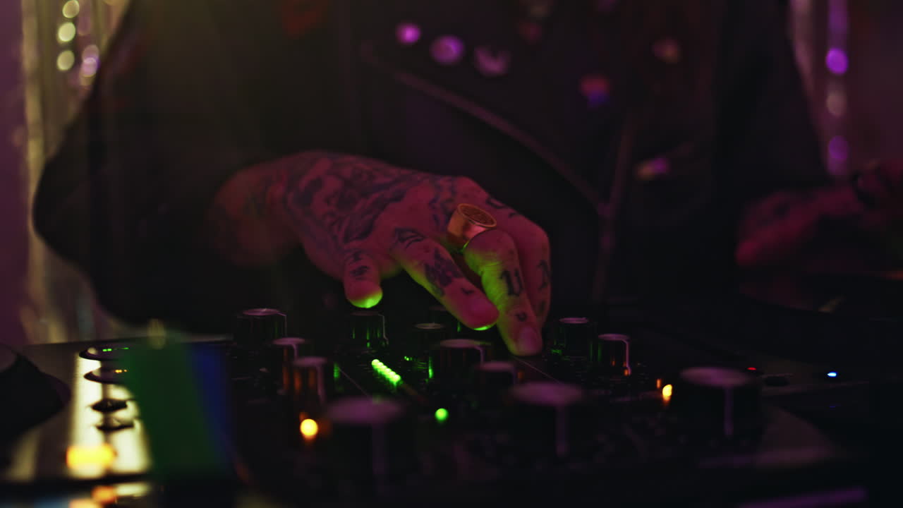 DJ tattooed hand adjusting controller in neon lights closeup. Woman disc jockey