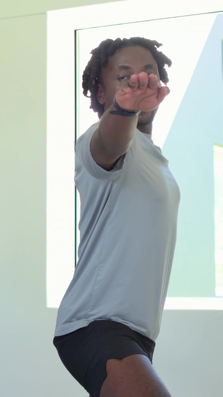 Vídeo vertical: Homem de shorts começando a se equilibrar, abaixando a perna e respirando em casa com uma faixa