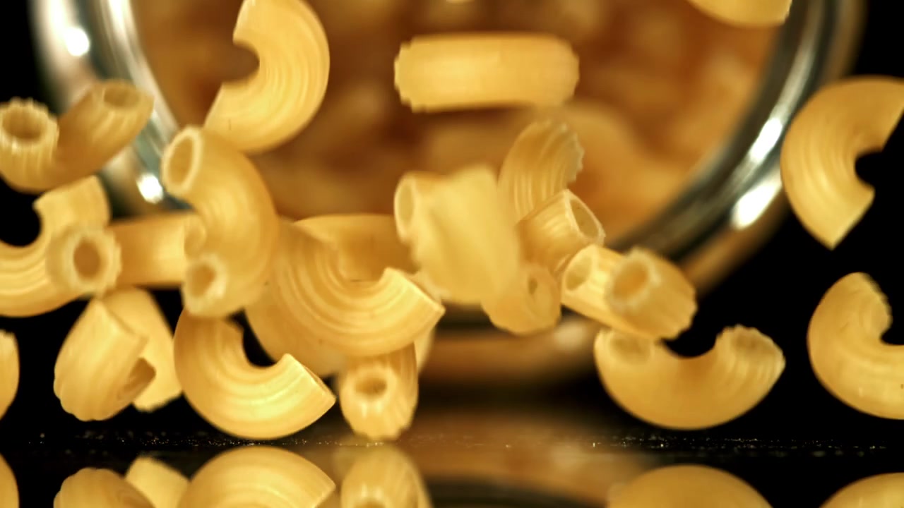 Pasta maccheroni secca che cade al rallentatore su sfondo nero.