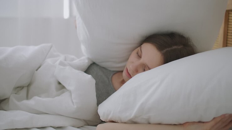 The annoyed woman woke up early in the morning from extraneous noise. Woman covers herself with pillows so as not to hear noise in the bedroom early in the morning