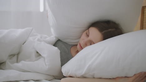 the annoyed woman woke up early in the morning from extraneous noise. woman covers herself with pillows so as not to hear noise in the bedroom early in the morning