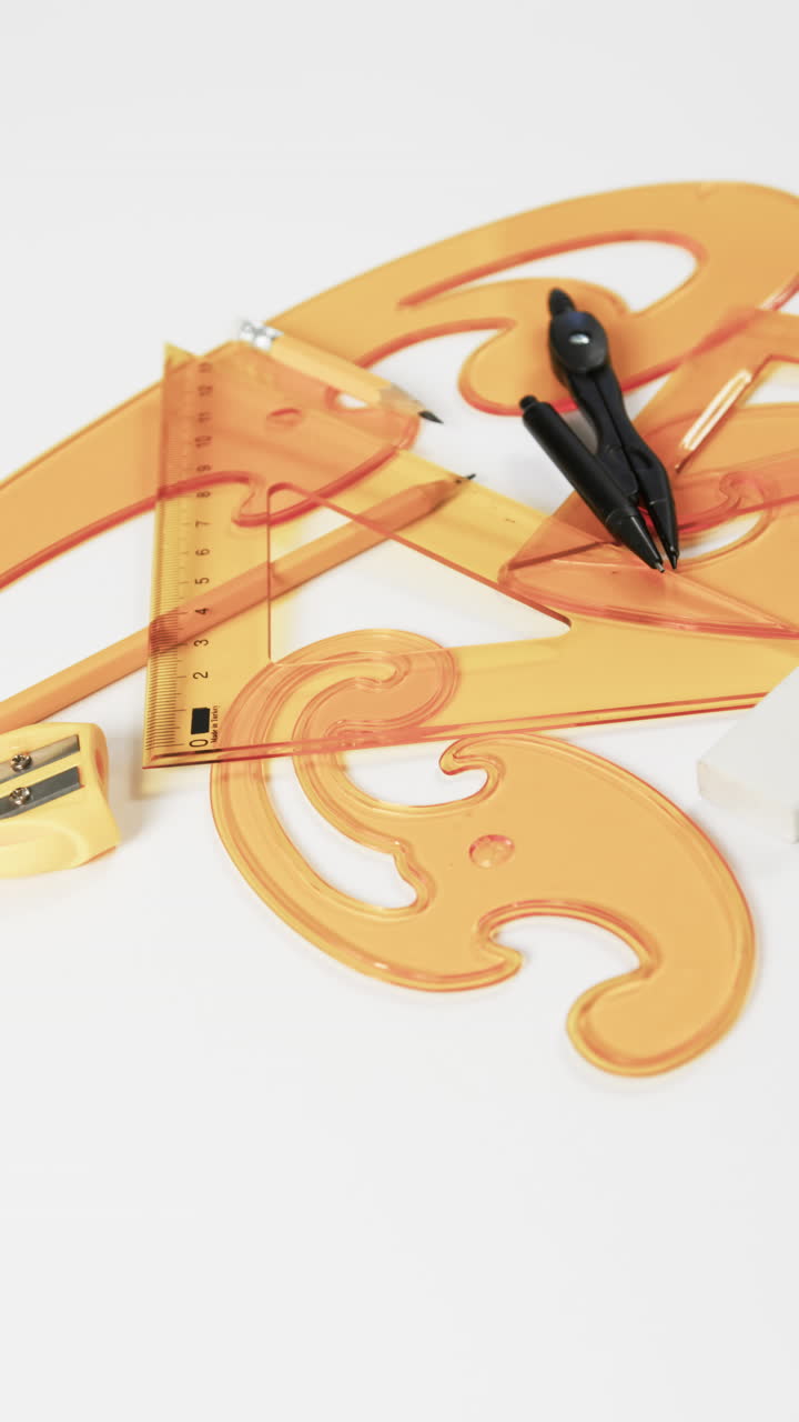 Vertical video of compass, pencil, sharpener, eraser and rulers on white background, slow motion