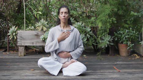 mujer biracial enfocada practicando meditación de yoga en un jardín soleado, cámara lenta