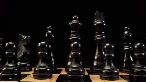 truck shot from right to left of black chess pieces standing on a chessboard on a black background