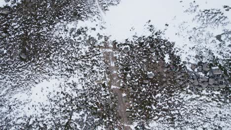 Aerial-drone-footage-in-winter-filmed-in-Coire-an-t-Sneachda-in-the-Cairngroms-National-Park-in-Scotland-with-patchy-snow-in-the-mountains,-looking-down-towards-an-icy-hiking-trail-and-and-boulders