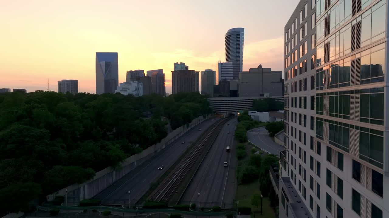 Drone shot reveals metropolitan Atlanta Georgia area, Buckhead skyline and skyscrapers at sunset, Subway train station and road traffic with urban city buildings
