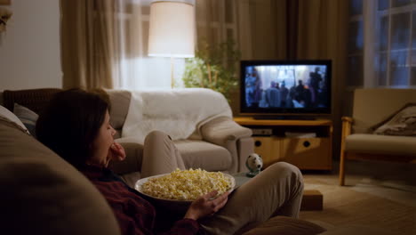 woman watching tv and eating popcorn at home