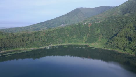 Aerial-view-of-green-lake-among-mountain-cliffs-and-forest