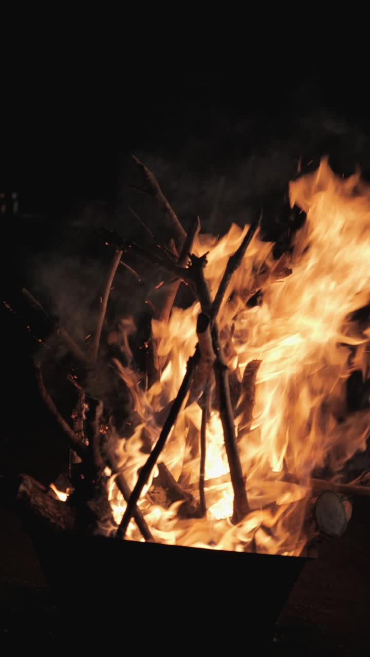 A warm bonfire burning outdoors, shot in vertical slow motion, with glowing flames and wood