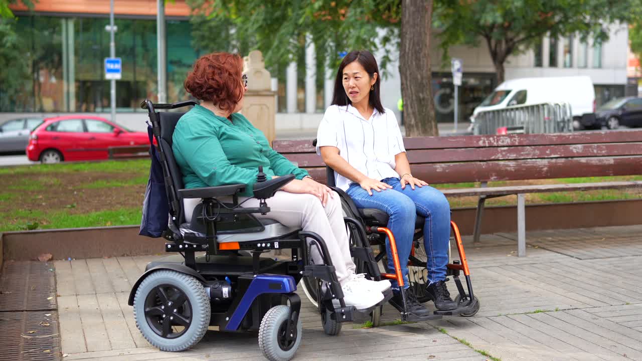 Two women in wheelchairs conversing on a city street