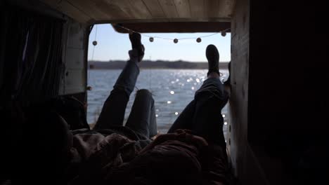 two girls are lying in the back of a caravan by a lake. they have a beautiful view.