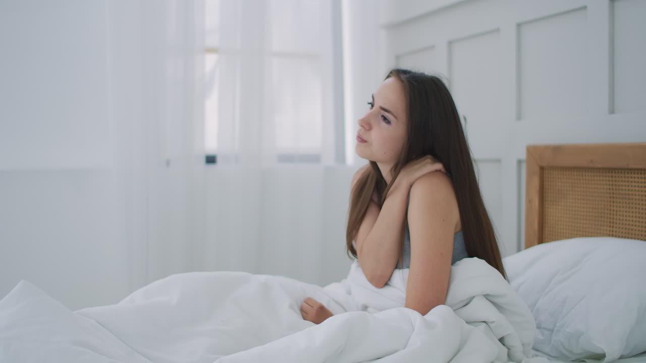 여성이 깨어나고 어깨와 목에 통증이 있습니다. 혼란스러운 여성은 침대에서 깨어나 목 등에 통증이 있습니다.