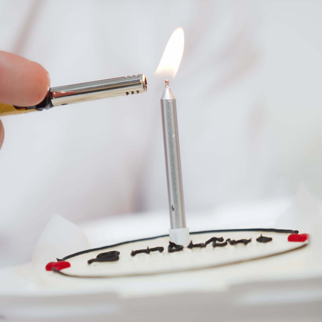 Male hand lights the candle in a cake. Celebration cake close up. White backdrop