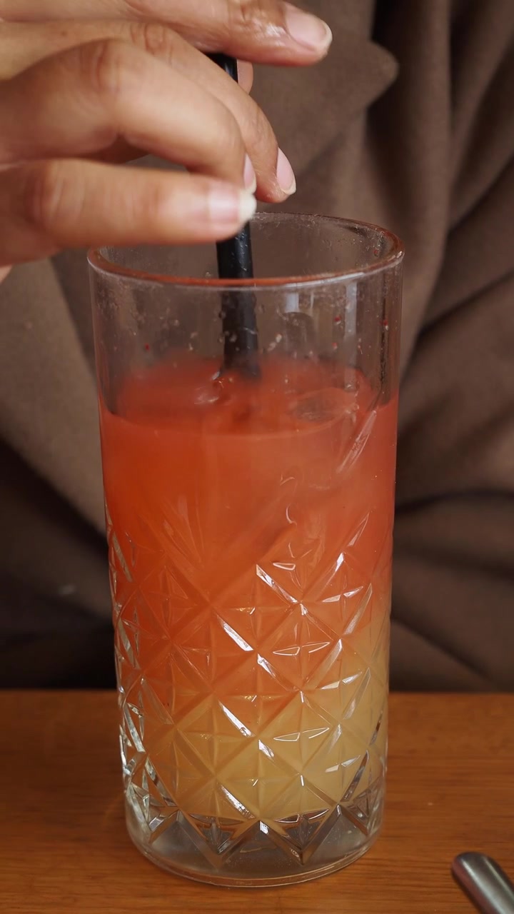 Persona che mescola un cocktail stratificato rinfrescante con una cannuccia