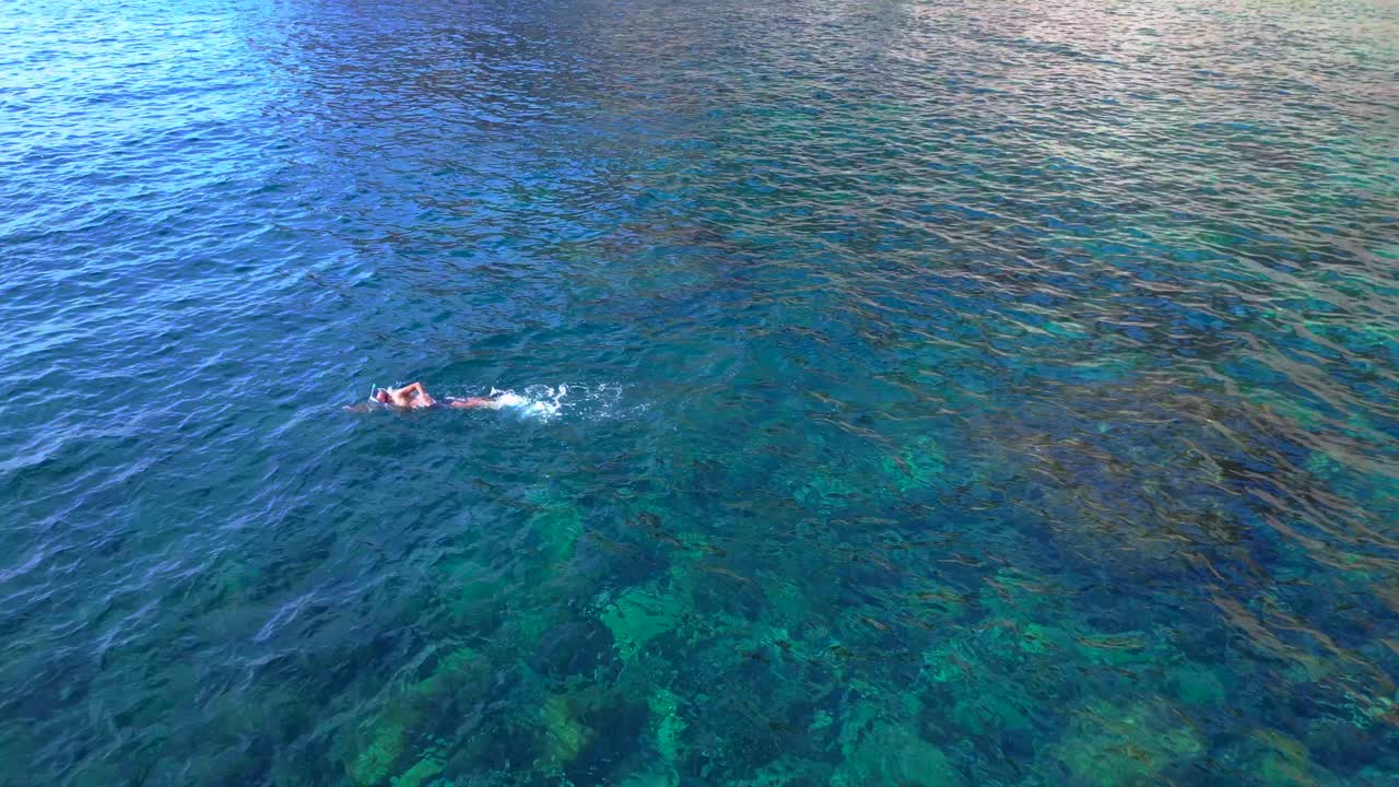 Male tourist swimming in the transparent waters of a bay in Ibiza, Spain. Dramatic aerial view flight drone shot footage from above