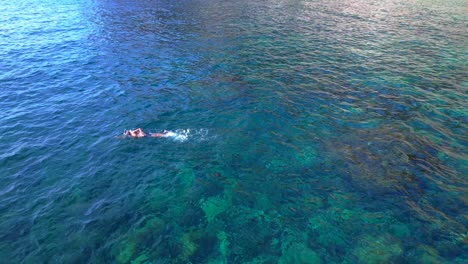 male tourist swimming in the transparent waters of a bay in ibiza, spain. dramatic aerial view flight drone shot footage from above