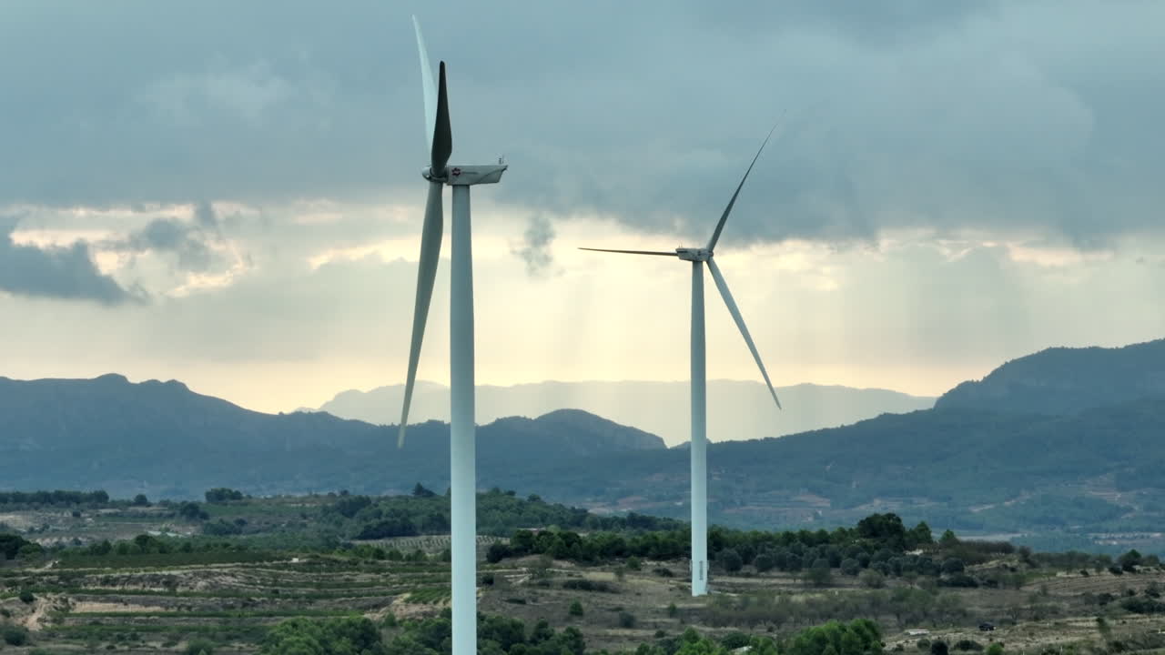 aerogeneradores inoperativos y paisaje montañoso de coll de moro en segundo plano con cielo tormentoso nublado, cataluña en españa