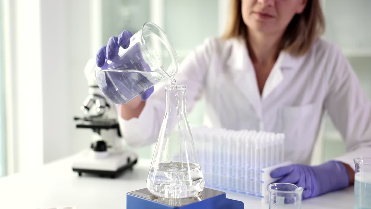 Female laboratory technician pours clean water into flask
