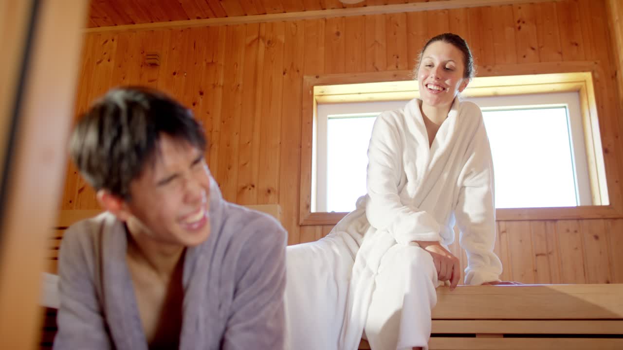 Diverse couple sharing smiles while woman leaning forward starting chat to rest on spa seats robes