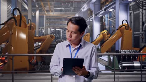 asian male professional worker standing with his tablet with industrial robotic arms working, he is nodding his head with dissapionted