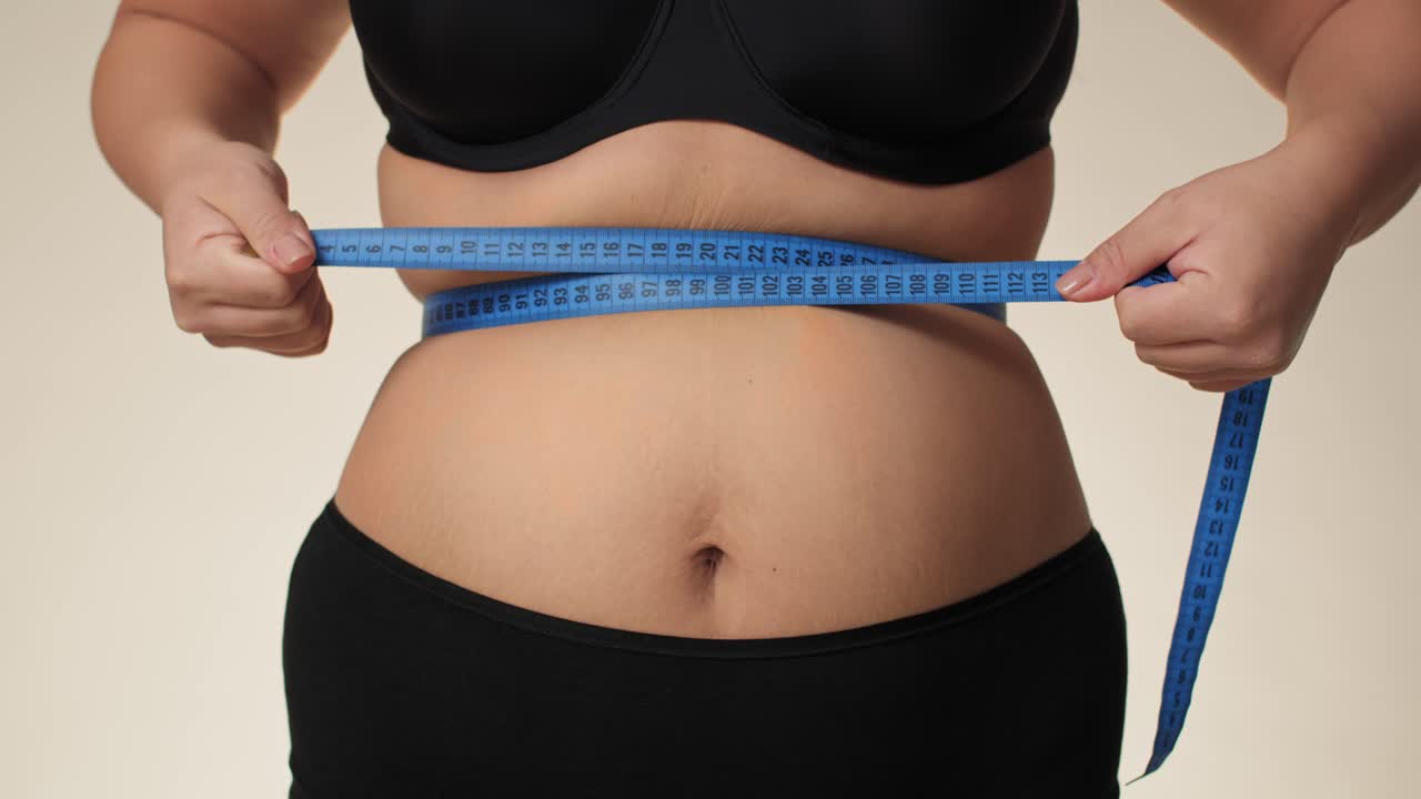 mujer de talla plus irreconocible en ropa interior midiendo su cintura con cinta métrica.