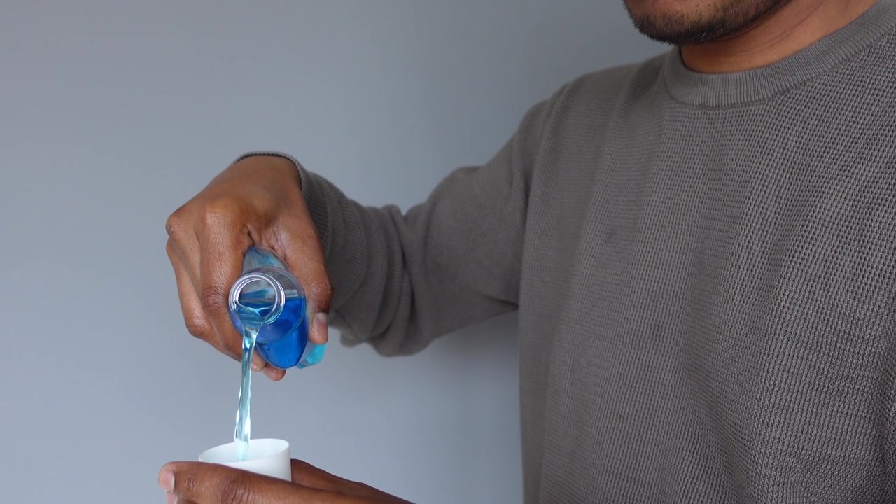 Persona vertiendo enjuague bucal azul en una pequeña taza medidora.