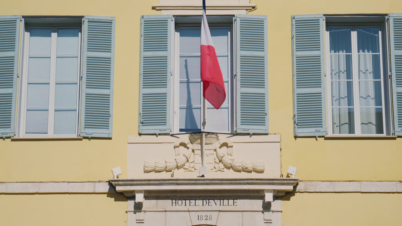 Vista dettagliata dell'Hotel de Ville, con la bandiera francese appesa sopra l'ingresso, persiane blu, elegante decorazione in pietra e l'iscrizione "Hotel de Ville 1828", Antibes, Francia