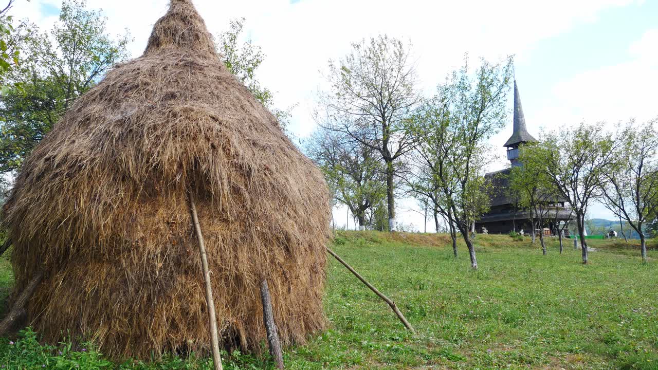 toma panorámica de un montón de paja y una iglesia de madera en una zona rural.
