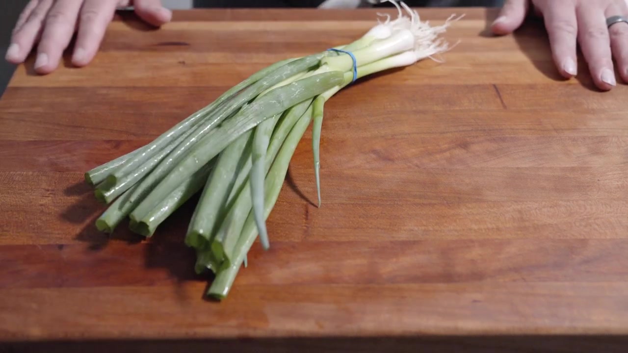 Una ripresa dall'alto al rallentatore delle mani di uno chef mentre gli scalogni vengono fatti cadere su un tagliere. Catturato in 4K a 120fps, il clip evidenzia la precisione nella preparazione del cibo con qualità cinematografica.