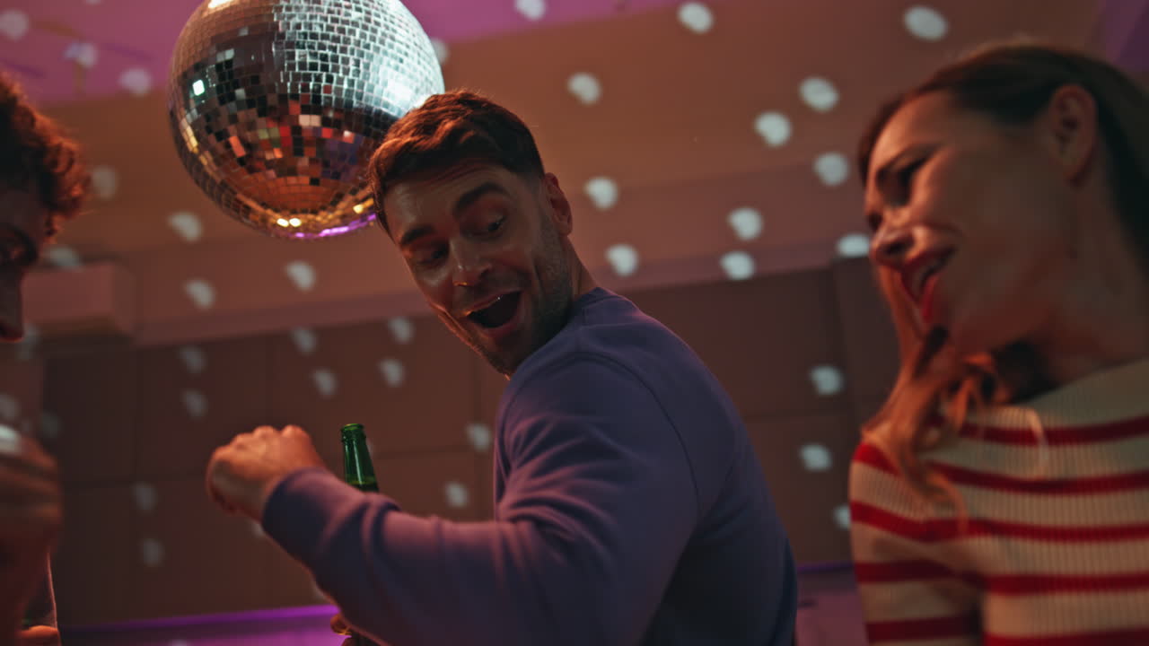 Joyful students dancing night party with beer bottles close up. Smiling people