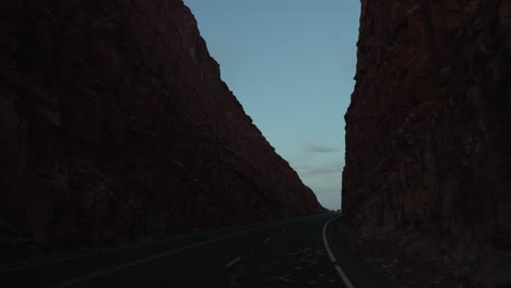 In-Der-Abenddämmerung-Eine-Wüstenstraße-Zwischen-Hohen-Felswänden-Hinunterfahren---Konzept:-Dunkle-Straße,-Unheimlich,-Allein,-Entdeckung,-Erkundung,-Roadtrip,-Camping