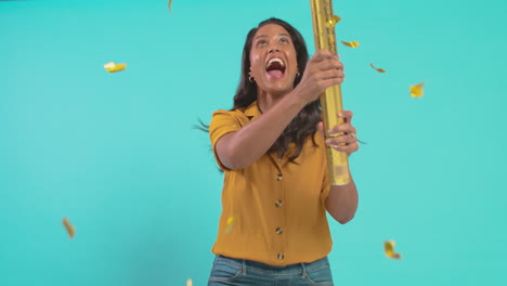 excited mature woman celebrates winning firing gold confetti canon in studio against blue background