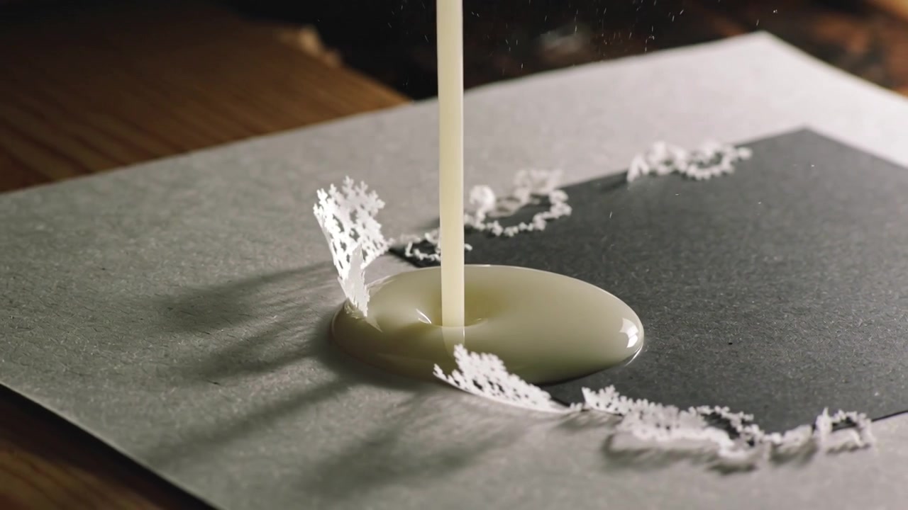 暗いカードの上に上からとろみのある液体を注ぎ、光沢のある水たまりを作りながらレースの縁を濡らす
