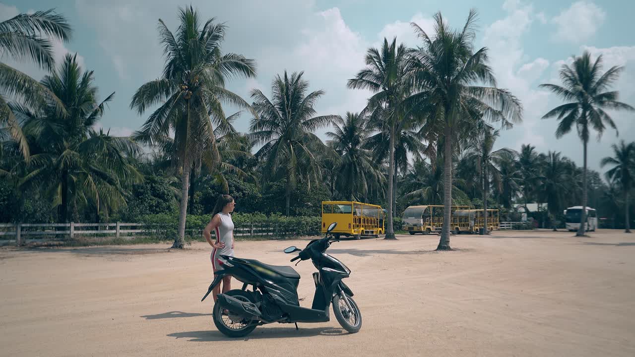 소녀는 인상적인 검은 모터 자전거로 큰 광장에 서 있습니다.
