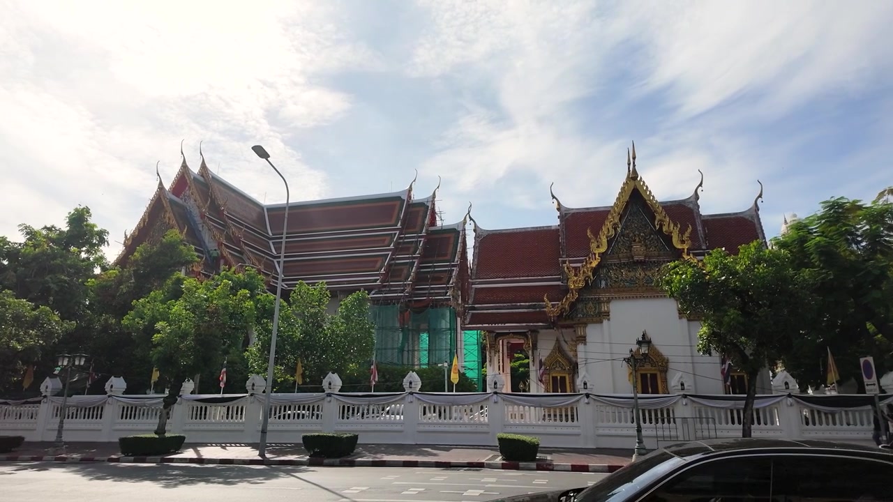 Ampia inquadratura di edifici di templi ornati e traffico stradale sotto un cielo soleggiato a Bangkok