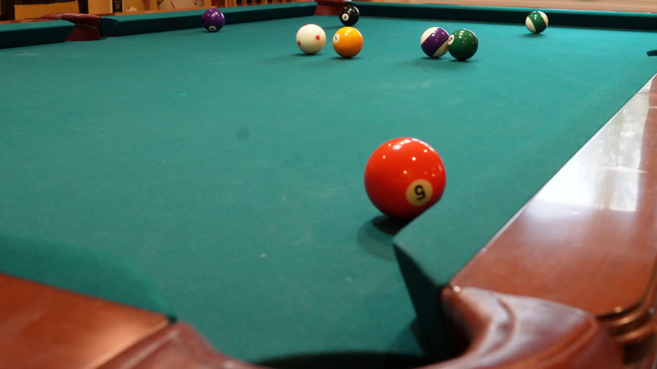 Man Playing 8 Ball Pool Shoots Several Solid Balls into Pockets on a Brunswick Table with Green Felt Missing a Shot at the End, Open Bridge Hand and Wooden Cue Stick, Low Angle no faces
