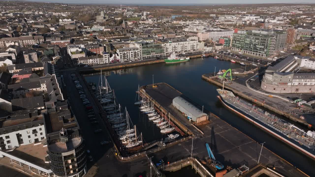 Ripresa con drone dall'alto del Porto di Galway che mostra yacht e barche a vela ormeggiati, e il paesaggio urbano circostante della città di Galway, Irlanda. Ideale per contenuti di viaggio e immobiliari.