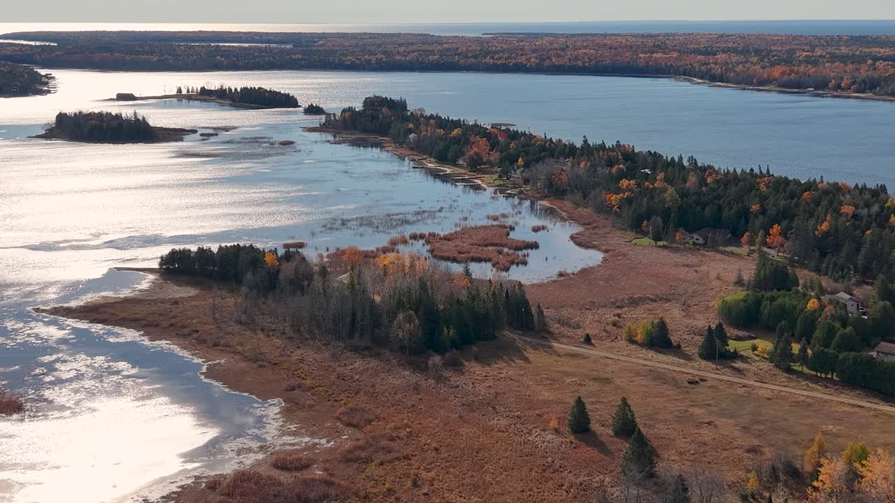 Aerial drone shot over a rugged shoreline and inland forest meeting shimmering blue lake water in autumn