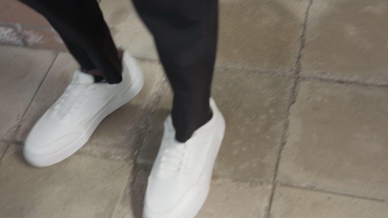 Elegant close view shows dark legs in white sneakers descending stairway, steady steps with relaxed rhythm, denim hem brushing ankle, mood centered on shoe movement and graceful pace