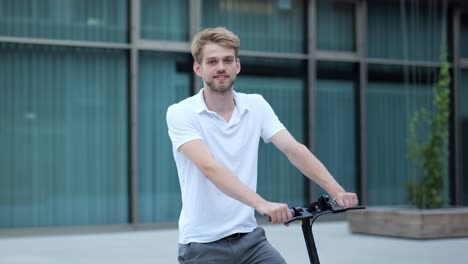 joven empresario de pie en su e-scooter y sonriendo a la cámara