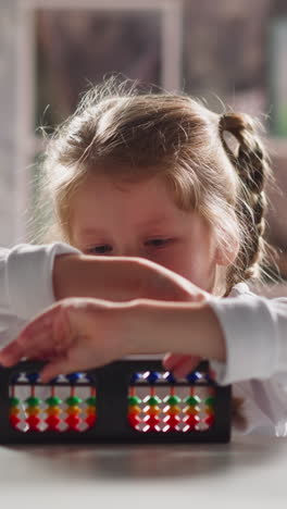 curious little girl turns and looks at colorful abacus experimenting at table during mental mathematics lesson in kindergarten close view slow motion