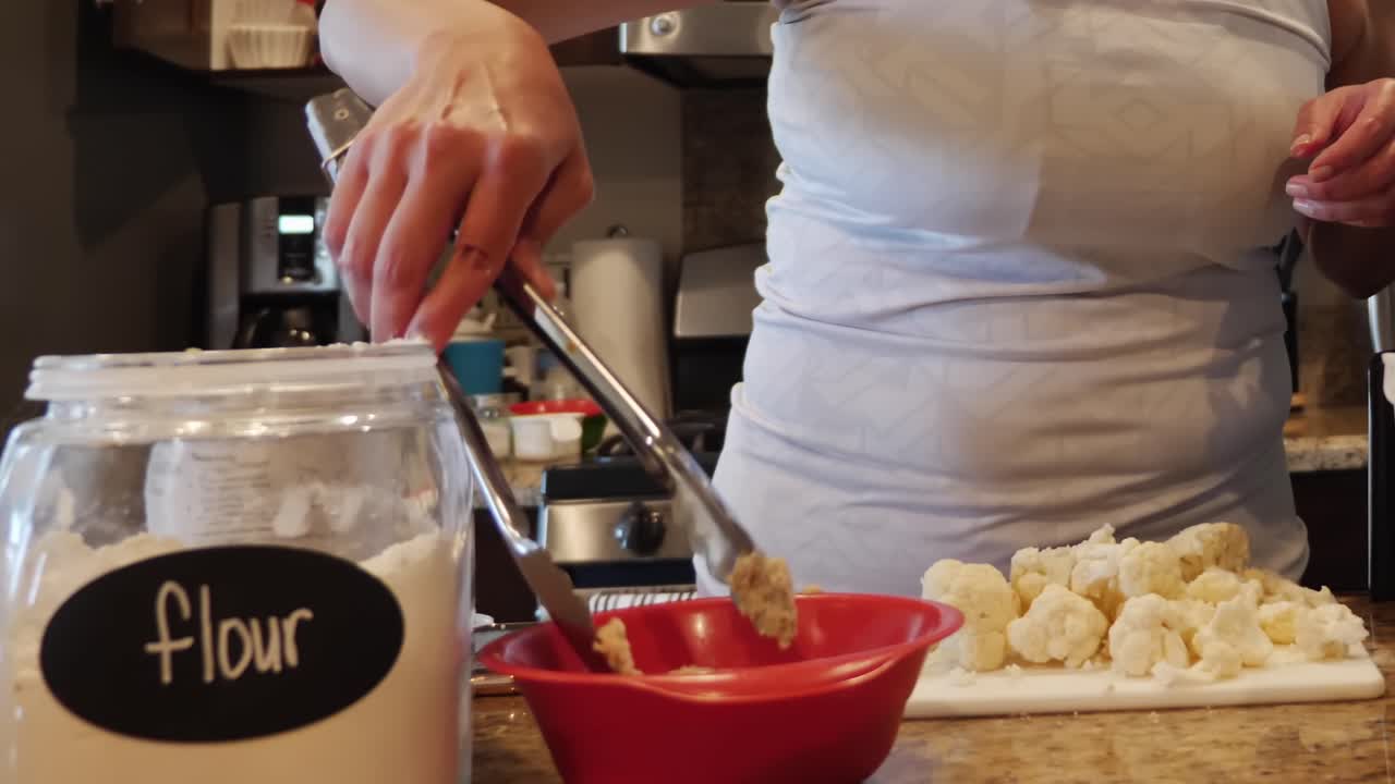 Woman chef putting batter mix on chopped cauliflower at home