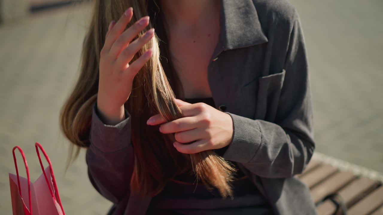 primer plano de una mujer con una camiseta negra bajo una camisa gris, tocando su cabello lúdicamente, con una vista parcial de la bolsa de compras roja es visible a su lado con el fondo ligeramente borroso